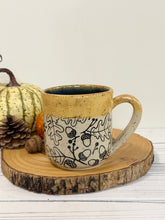 Load image into Gallery viewer, #001 - 16 oz. Leaf and acorn patterned speckled mug with burnt yellow rim and dark blue inside
