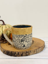 Load image into Gallery viewer, #001 - 16 oz. Leaf and acorn patterned speckled mug with burnt yellow rim and dark blue inside
